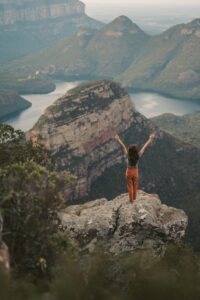 A person standing tall on a mountain peak with open arms embracing .