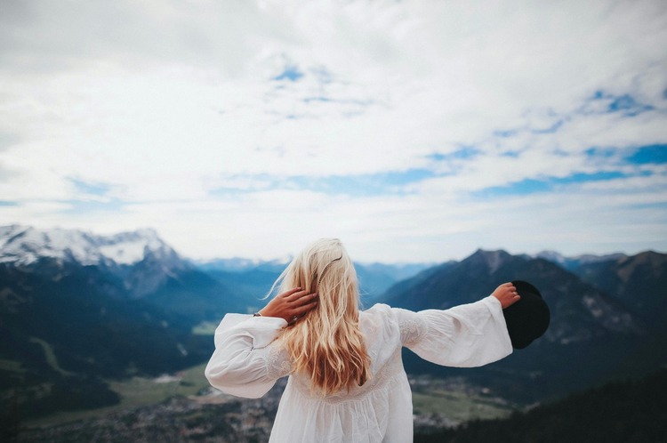A erson standing tall on a mountain peak with open arms embracing courage.